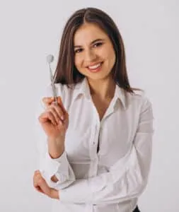 Confident woman in a white shirt holding a dental mirror, smiling at the camera.