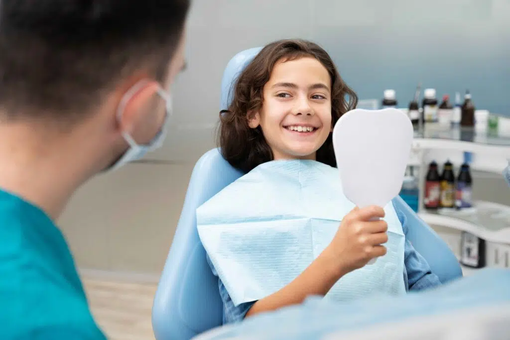 6 Powerful Advantages of Low Light Laser Therapy in Dentistry - Comprehensive Family Dental 9 Young girl smiling and holding a mirror after a dental checkup.