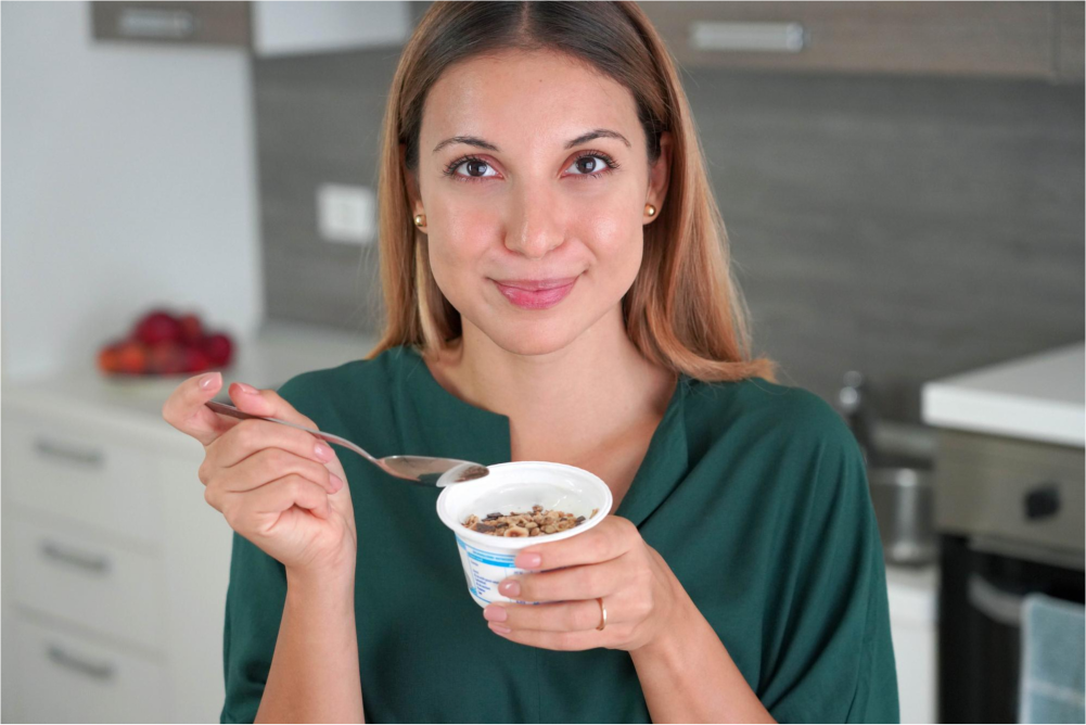 Woman eating yogurt in kitchen.