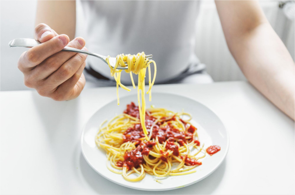 Person eating spaghetti with sauce.