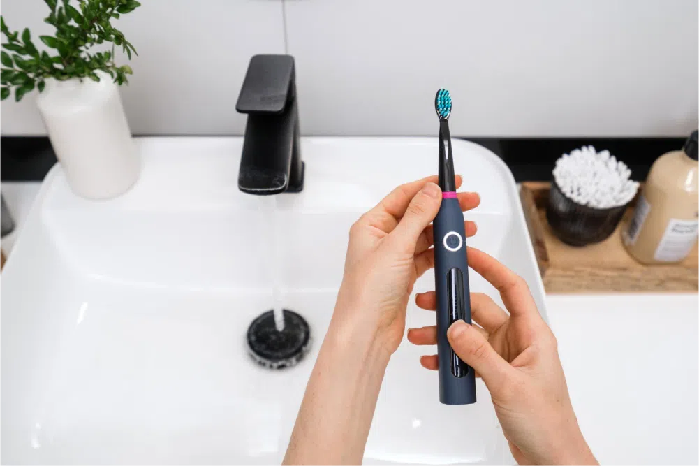 How To Floss With Braces 5 Holding electric toothbrush by sink