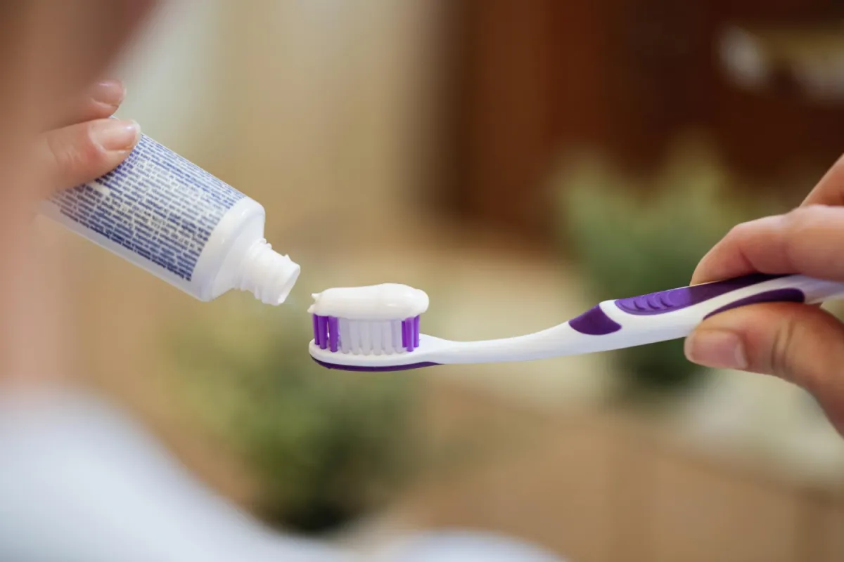 Person applying toothpaste onto toothbrush.