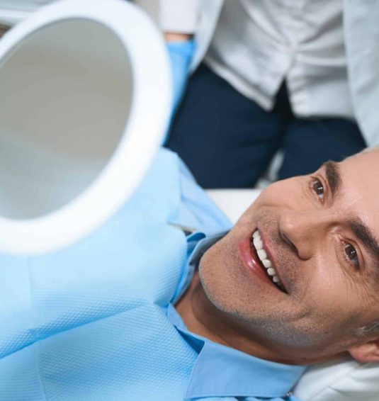 Man smiling, holding mirror, after dental procedure.